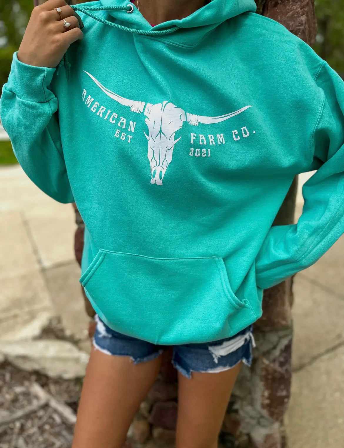 Close up picture of teal American Farm Company hoodie with white print including a bull skull and American Farm Company logo