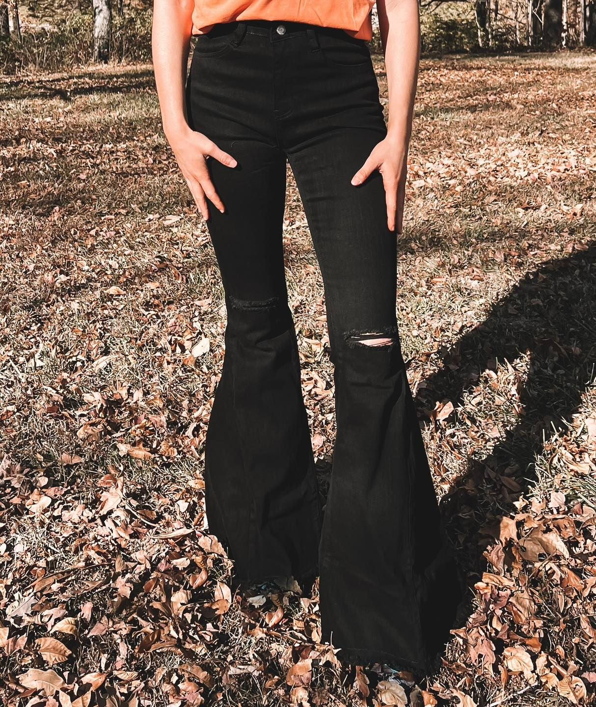 Close up image of black flare denim pants with distressing in the knee